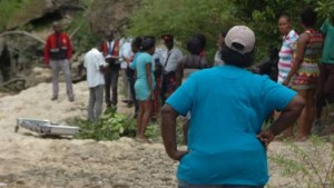 Angella Johnson-Maxwell (with back turned) stands a few metres from the site where her son’s body is covered under tree branches, while supportive residents talk with the police